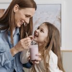 A joyful moment of a mother and daughter sharing a strawberry milkshake indoors.